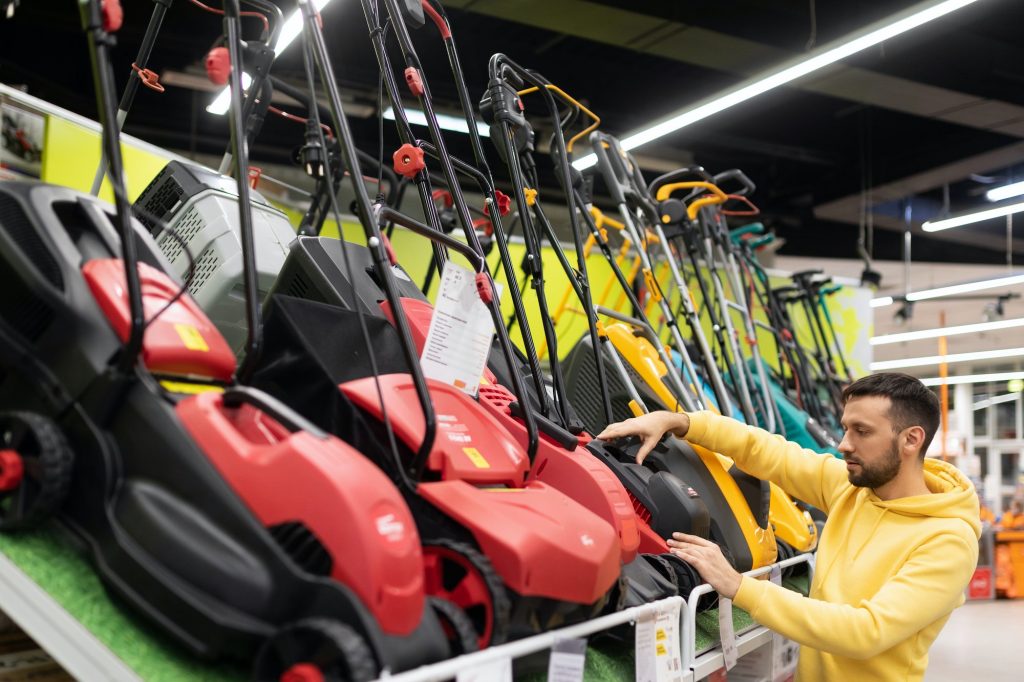 man examining petrol electric lawn mowers in garden equipment store